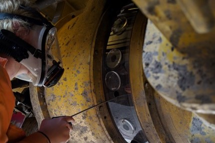 tradesperson using compressed air lance to clean alternator on mining truck through a sealed cover
