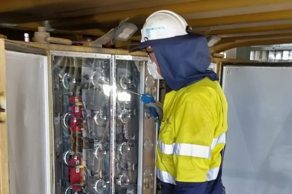 tradesperson using compressed air lance to clean electrical cabinets on mining truck through a sealed cover